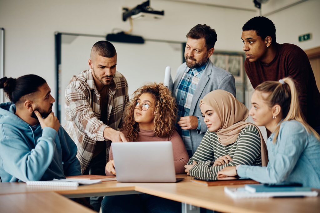 Multiracial group of college students and their teacher using computer in the classroom.